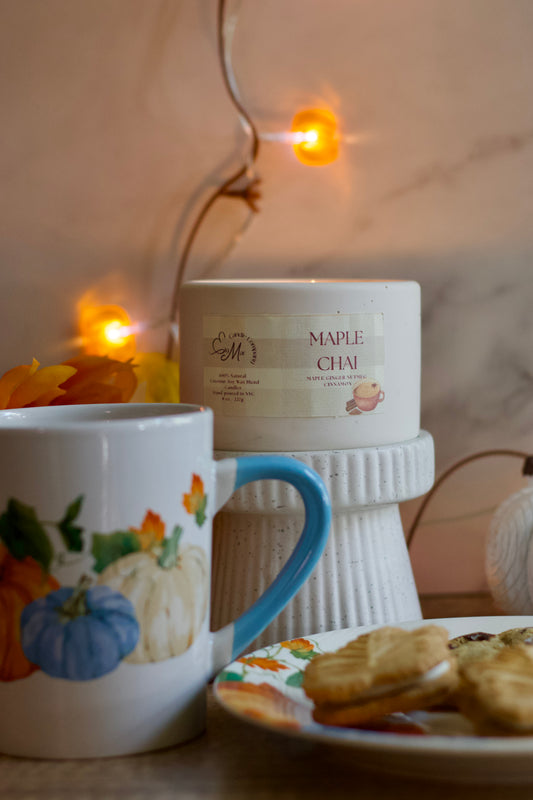 Cup with autumn-themed design, bowl of cookies, and candle on a decorative stand with warm lighting.