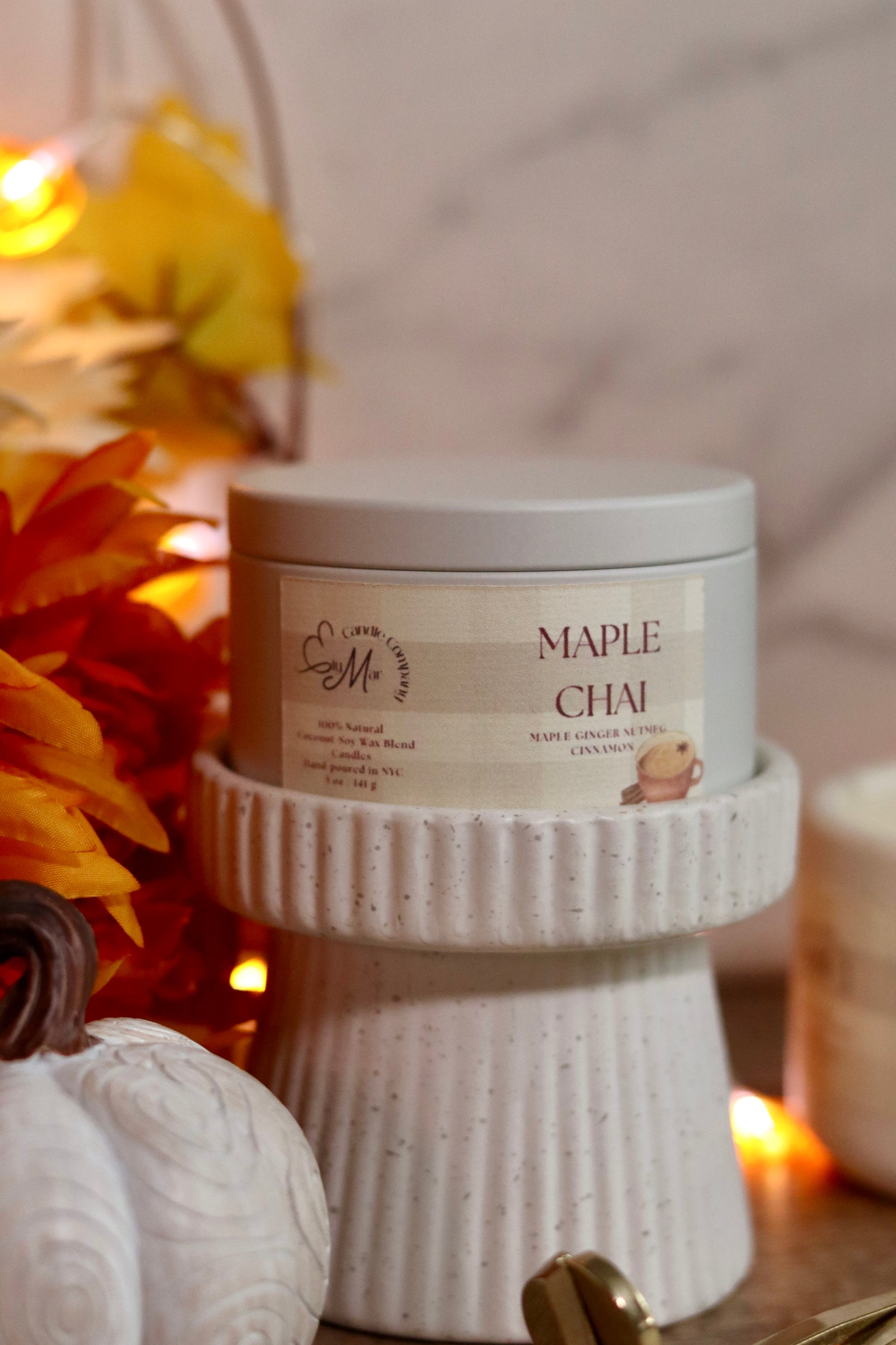 Candle labeled 'Maple Chai' on a textured stand with decorative elements in the background